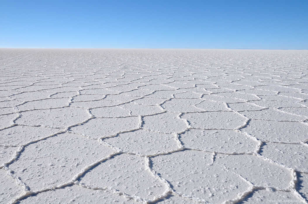 Die Salzkruste des Salar de Uyuni bricht in hexagonalen Formen auf und zieht sich bis zum Horizont hin.